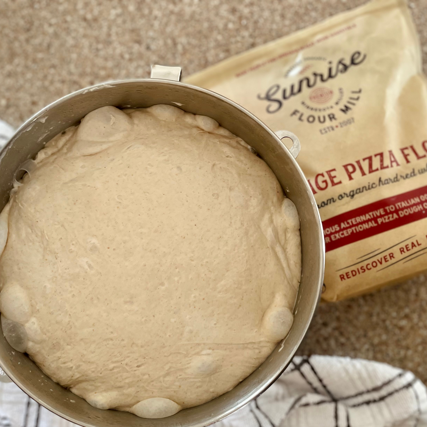 Proofed dough in a bowl next to pizza flour