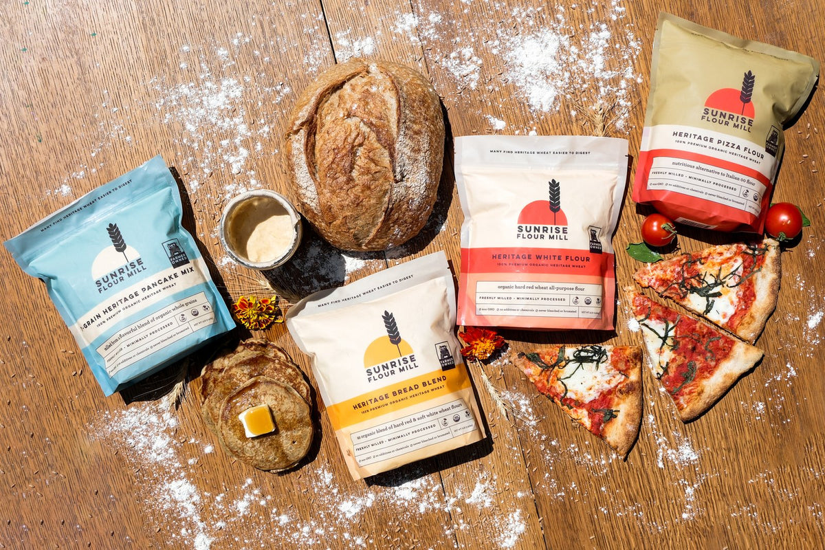 Heritage flour bags with a sourdough loaf, pancakes and pizza on a floured wooden table